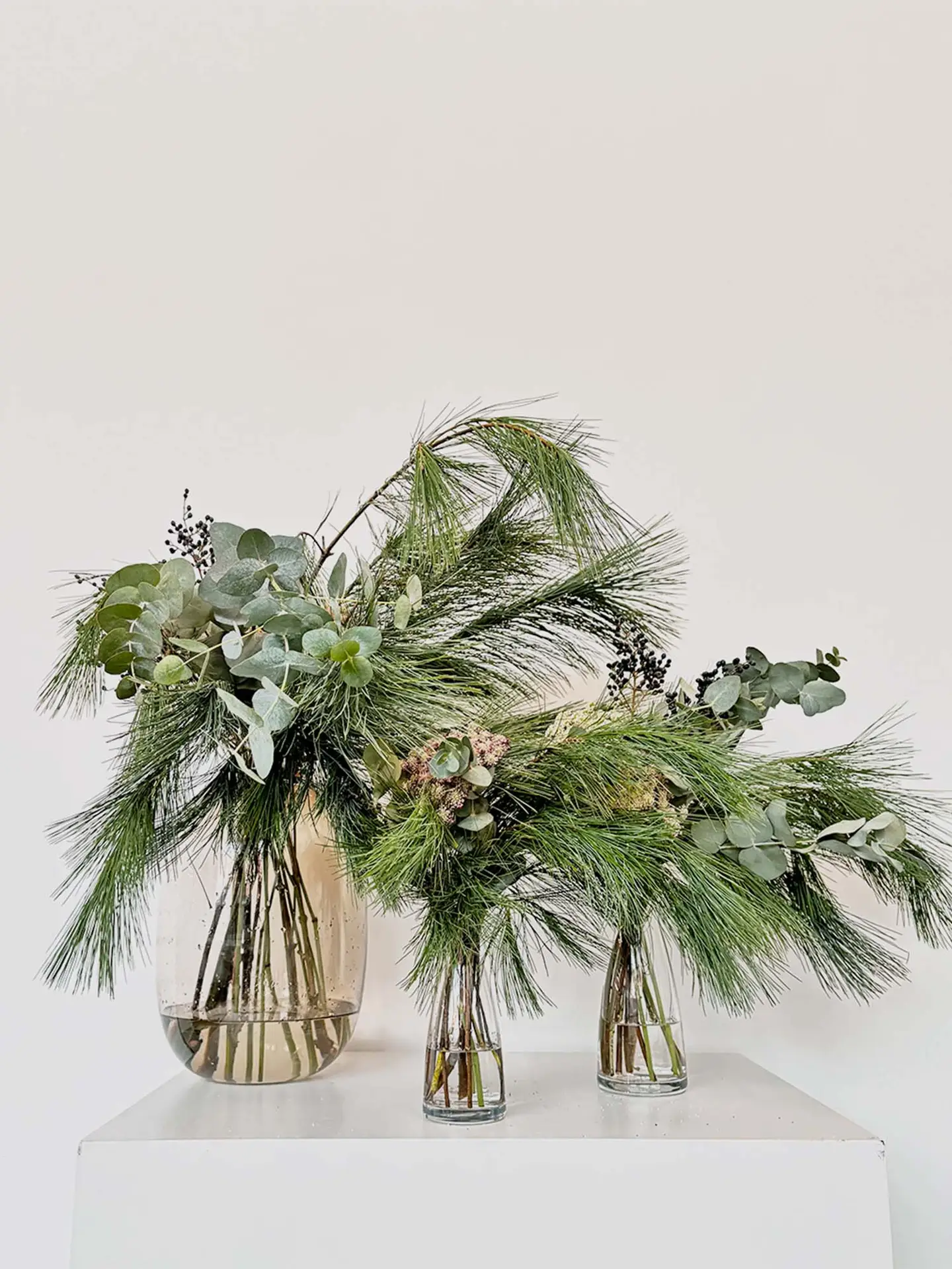 Ikebana Christmas arrangement with evergreen pine, eucalyptus, and seasonal greenery in glass vases — festive floral design by suminumi in Berlin.