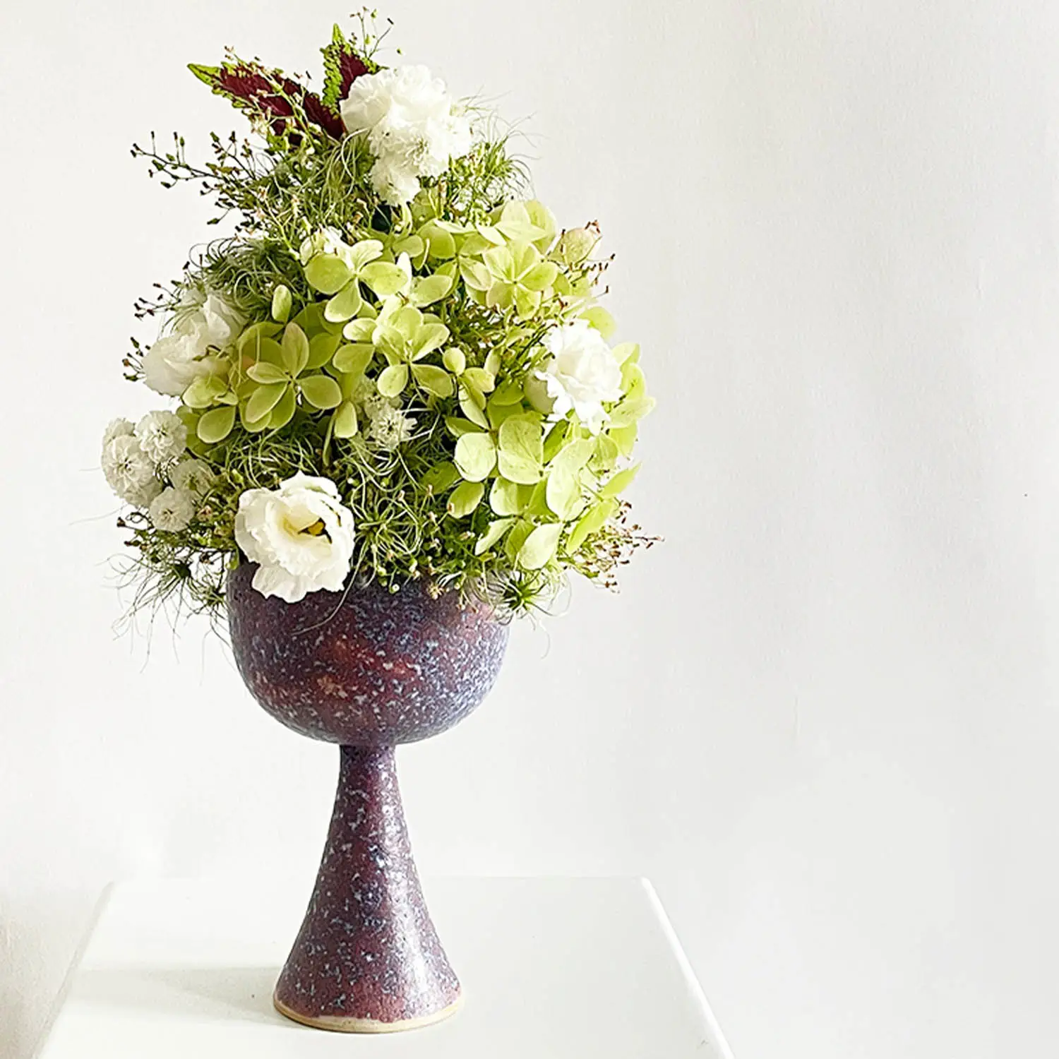 Elegant floral arrangement with green hydrangeas, white lisianthus, and delicate greenery in a tall pedestal vase, designed as a wedding celebration piece in Berlin by suminumi.