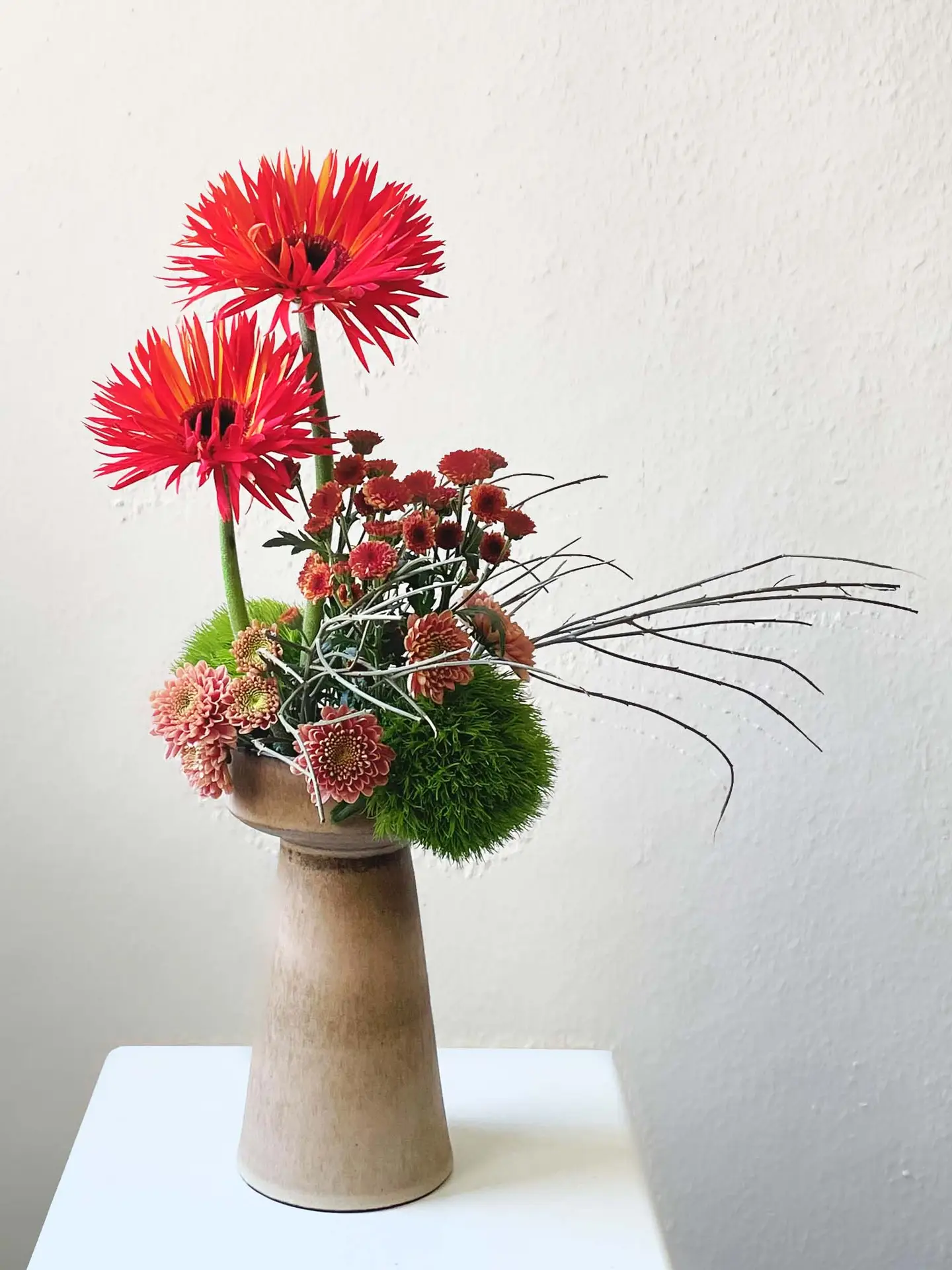 Flower arrangement with red gerbera, chrysanthemums, and moss balls in a tall pedestal vase by ceramic artist Verena De Hoog, created by suminumi in Berlin.