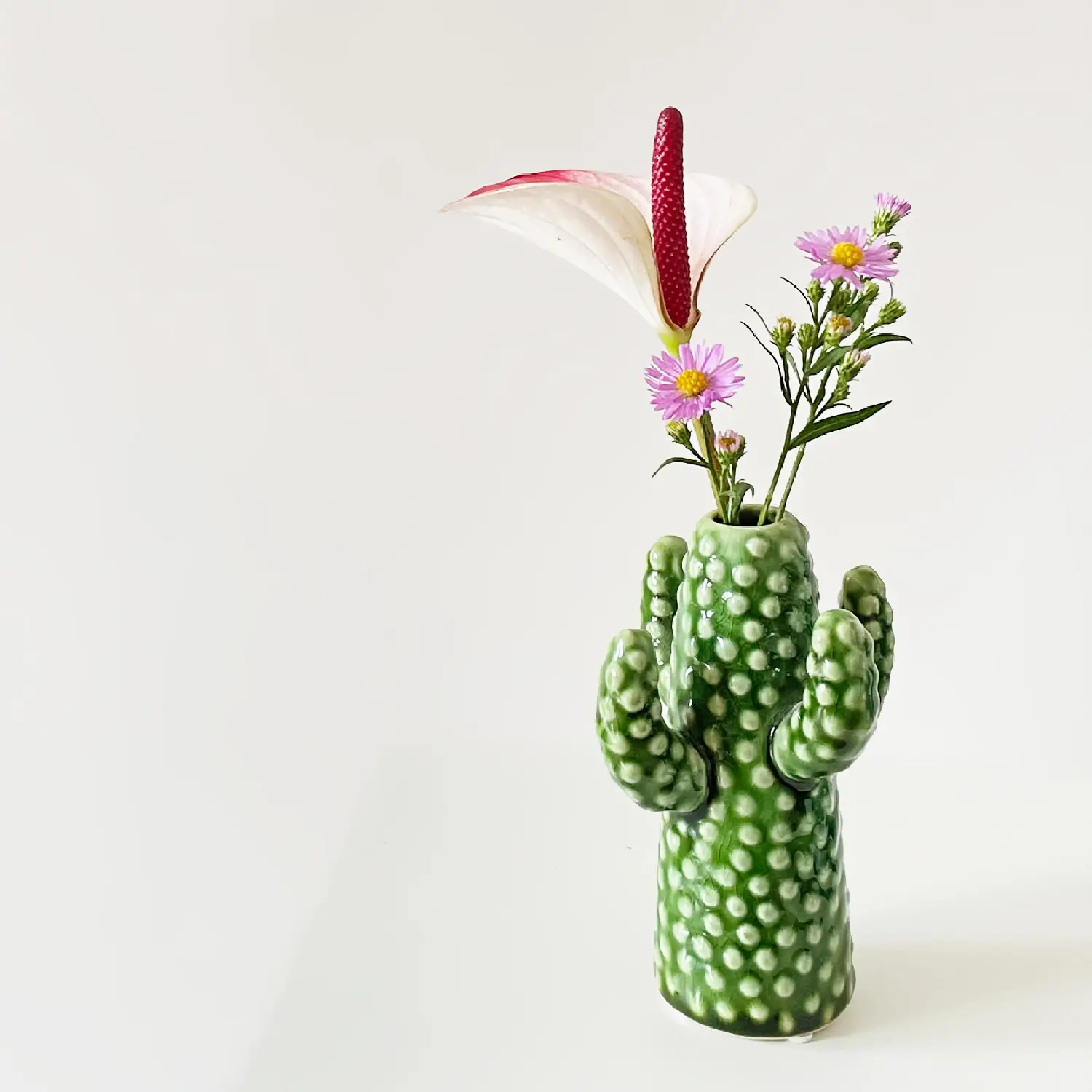 Ikebana arrangement with pink anthurium and purple daisies in a green cactus-shaped vase by Serax — contemporary Japanese flower arrangement