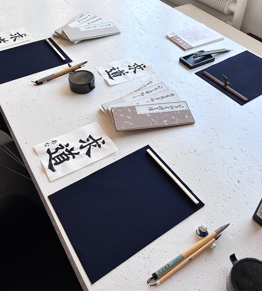 Shodō calligraphy workshop setup in Berlin with Japanese brushes, ink, practice paper and calligraphy samples on a white table.